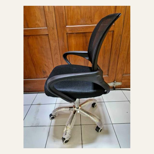 Kursi beroda hitam difoto serong dari sisi samping belakang di depan pintu kayu.
