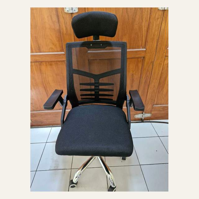 Kursi beroda hitam bersandaran kepala tampak depan dengan rangka punggung bercabang dan armrest datar.