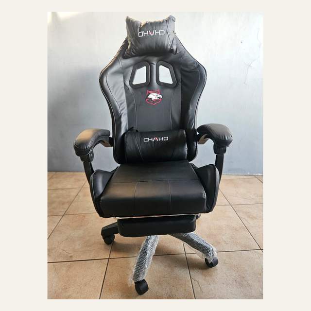 Kursi gaming hitam tampak depan dengan bantal kepala dan pinggang bertuliskan CHAHO serta sandaran kaki terlipat.