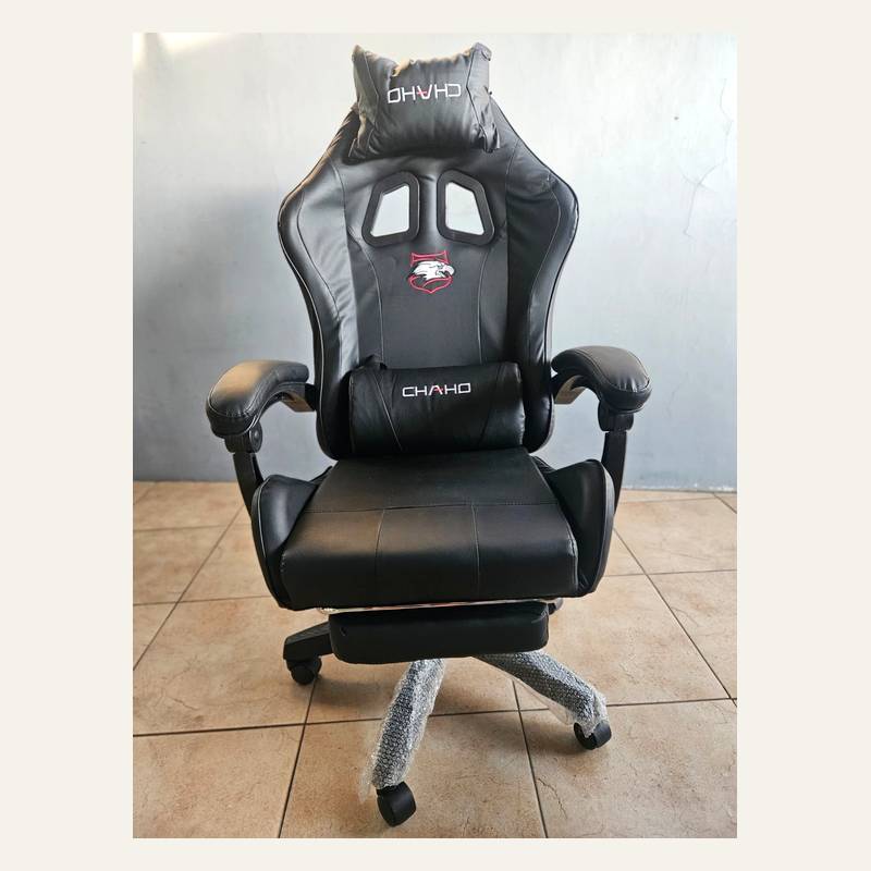 Kursi gaming hitam tampak depan dengan bantal kepala dan pinggang bertuliskan CHAHO serta sandaran kaki terlipat.