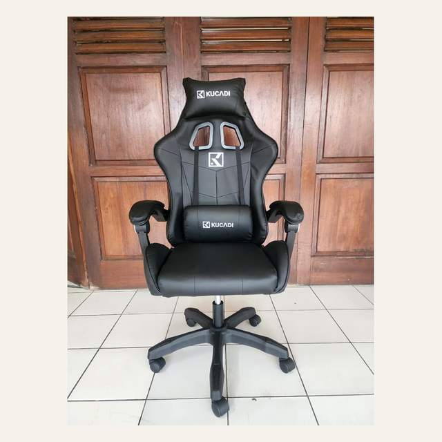 Kursi gaming hitam tampak depan dengan dua bantal bertuliskan KUCADI dan kaki lima cabang beroda.