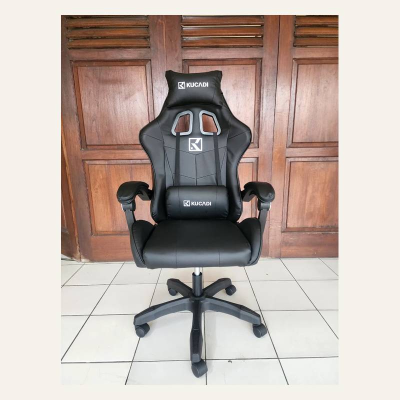 Kursi gaming hitam tampak depan dengan dua bantal bertuliskan KUCADI dan kaki lima cabang beroda.