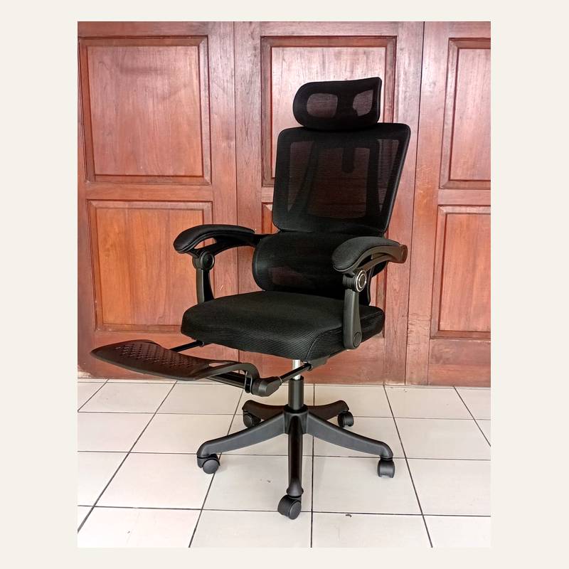 Kursi kantor hitam tampak serong dengan sandaran jaring, headrest, dan sandaran kaki terbuka ke samping.