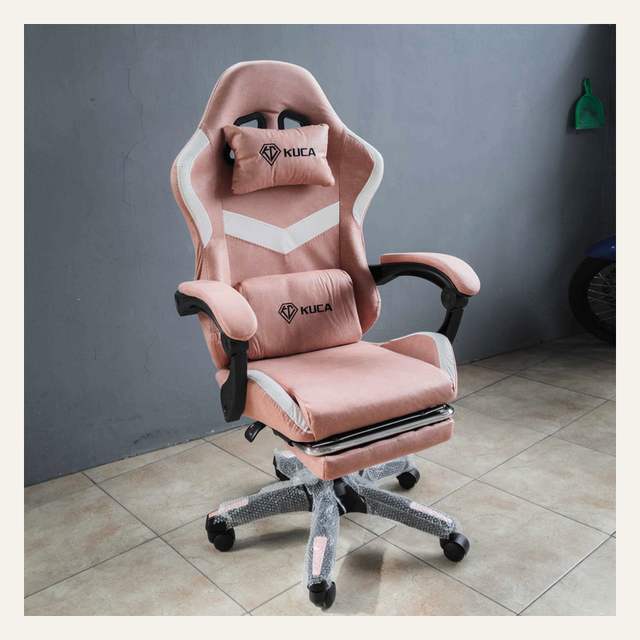 Kursi gaming merah muda tampak serong dengan bantal KUCA, sandaran kaki terbuka, dan kaki terbungkus plastik.