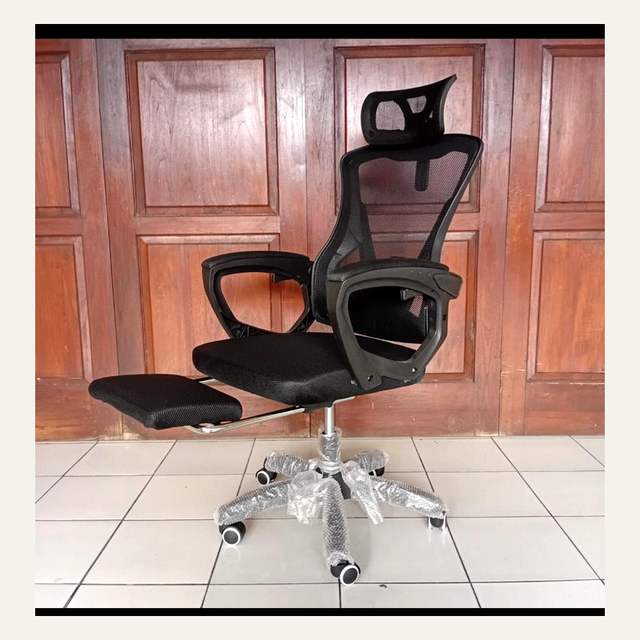 Kursi kantor hitam bersandaran jaring dengan sandaran kaki terbuka, difoto dari sudut serong.