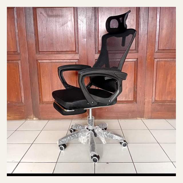 Kursi kantor hitam bersandaran jaring difoto dari sisi lain dengan sandaran kaki terlipat.