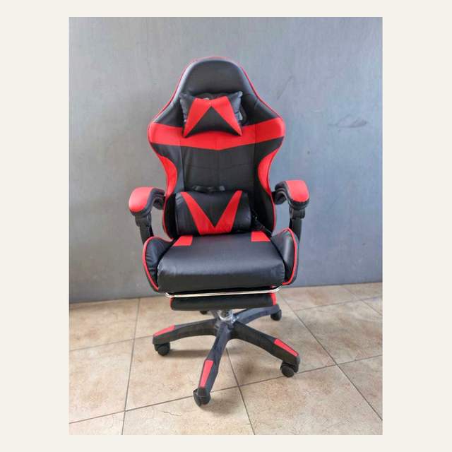 Kursi hitam merah dengan dua bantal difoto lurus dari depan di ruangan berdinding abu-abu.