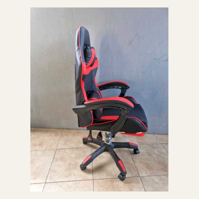 Kursi hitam merah difoto dari samping, memperlihatkan sandaran, bantal, dan kaki beroda.