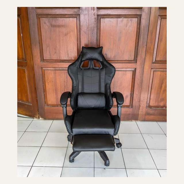 Kursi hitam polos difoto lurus dari depan dengan bantal leher, bantal pinggang, dan sandaran kaki.