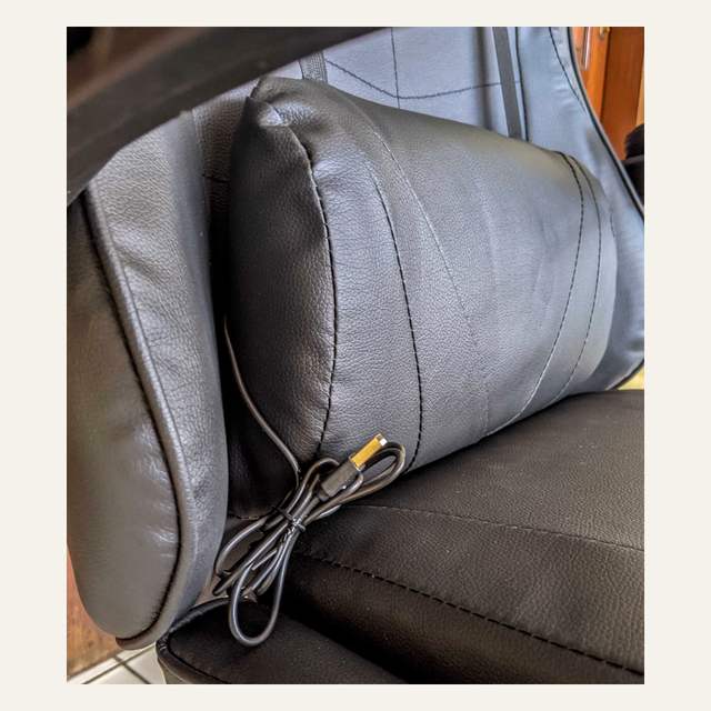 Foto dekat bantal pinggang hitam pada kursi dengan kabel terlipat dan konektor keemasan.