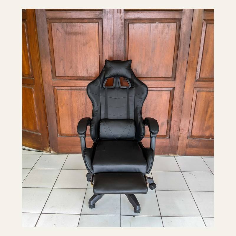 Kursi hitam polos difoto lurus dari depan dengan bantal leher, bantal pinggang, dan sandaran kaki.