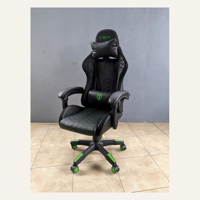 Kursi hitam beraksen hijau bertuliskan TITAN dengan bantal leher dan bantal pinggang, difoto serong.