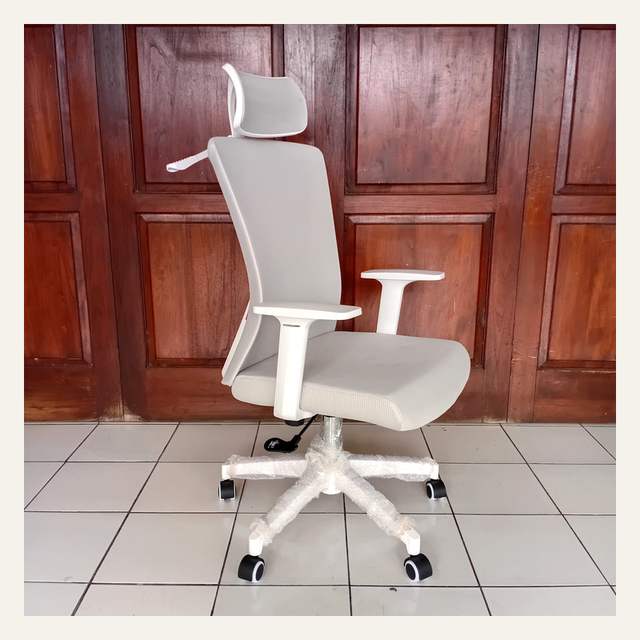 Kursi kerja putih abu-abu tampak serong di depan pintu kayu, kaki bintang terbungkus plastik gelembung.