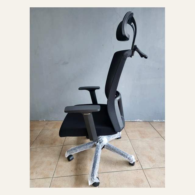 Kursi kerja hitam dilihat dari samping, sandaran melengkung dengan headrest di atas dan kaki bintang lima.