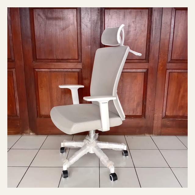 Kursi kerja putih abu-abu dilihat dari samping di depan pintu kayu cokelat, kaki terbungkus plastik gelembung.
