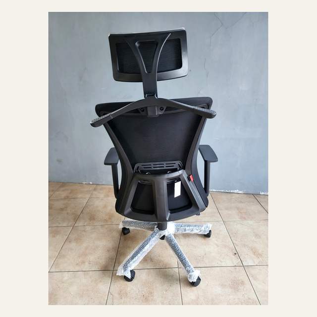 Kursi kerja hitam dilihat dari belakang, tampak rangka sandaran, label gantung, dan kaki bintang lima terbungkus.