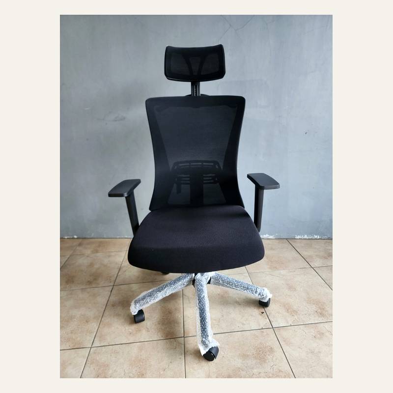 Kursi kerja hitam beroda tampak depan dengan sandaran jaring dan headrest, kaki masih terbungkus plastik gelembung.