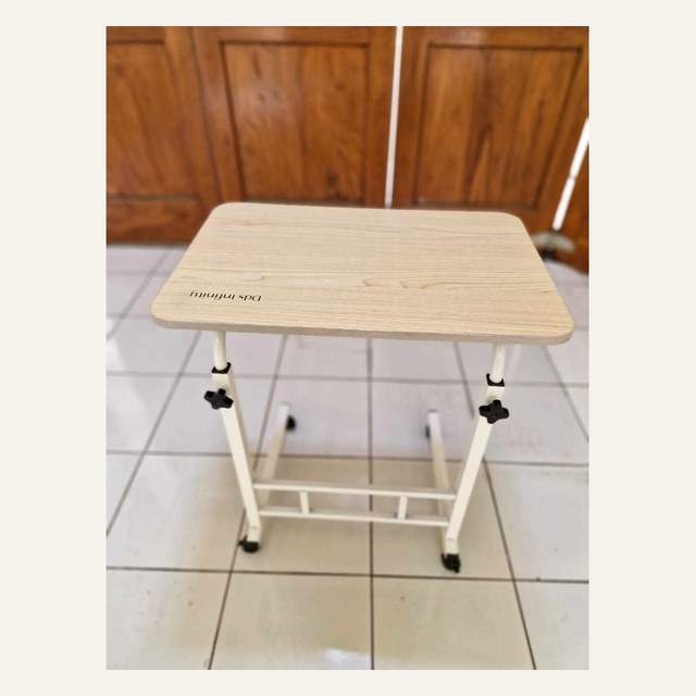 Meja kecil bermotif serat kayu terang dengan rangka putih, knob putar hitam, dan roda kecil di kaki.