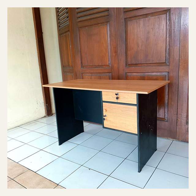 Meja kerja bermotif serat kayu dengan panel hitam dan dua laci berkunci di sisi kanan.