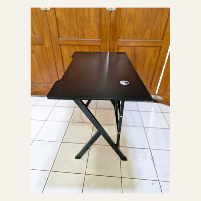 Meja cokelat tua difoto dari sudut samping memperlihatkan kaki hitam yang menyilang.