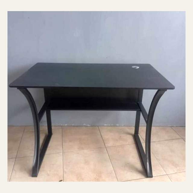 Meja hitam berkaki lengkung dengan satu rak bawah difoto dari depan di ruang berdinding abu-abu.