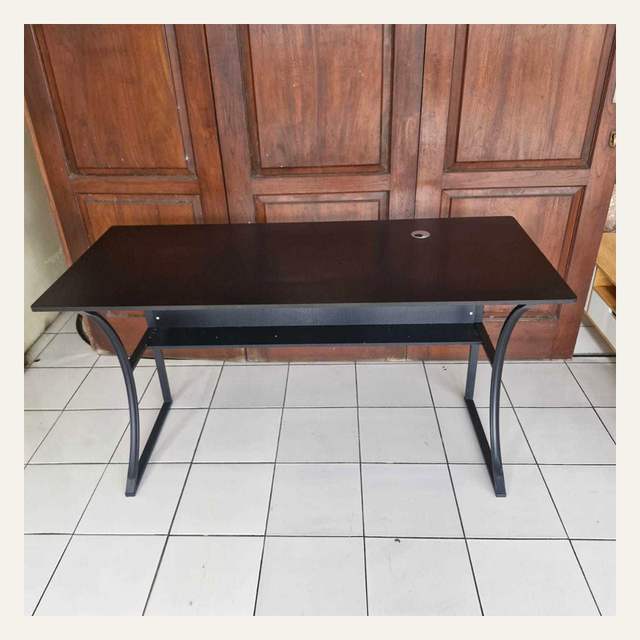 Meja permukaan cokelat tua berkaki hitam melengkung dengan rak bawah difoto dari depan.