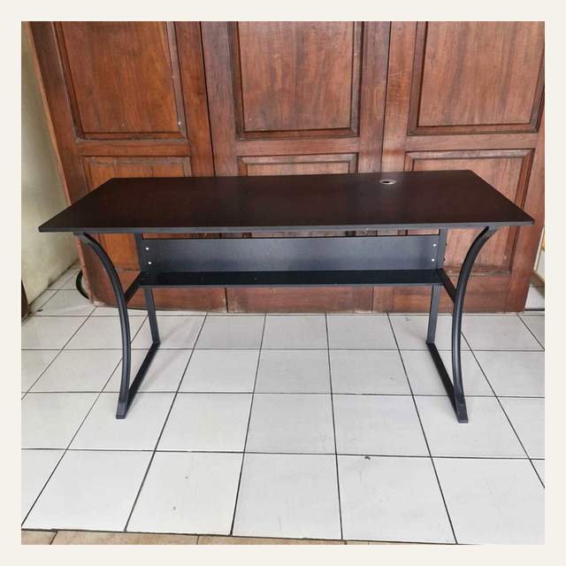 Meja cokelat tua dengan rak bawah dan kaki hitam melengkung berdiri di lantai keramik putih.