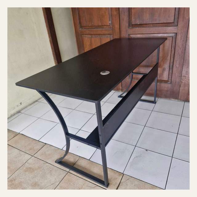 Meja bertepi cokelat tua dengan rak bawah dan kaki hitam melengkung difoto menyerong.