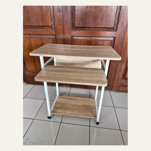 Rak tiga papan motif serat kayu terang dengan rangka putih dan roda kecil di lantai keramik.