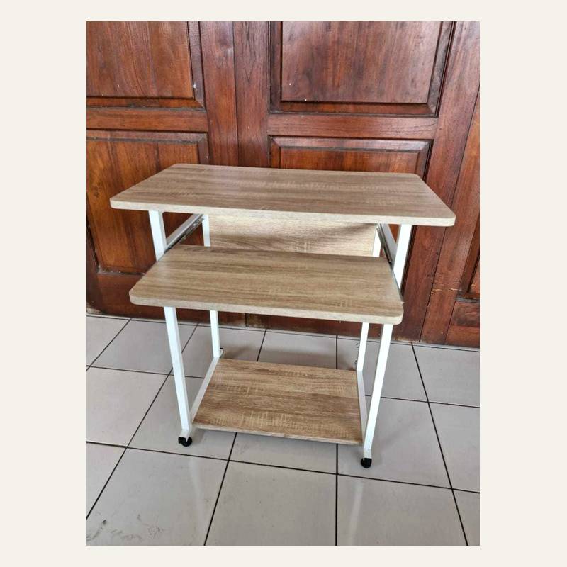 Rak tiga papan motif serat kayu terang dengan rangka putih dan roda kecil di lantai keramik.