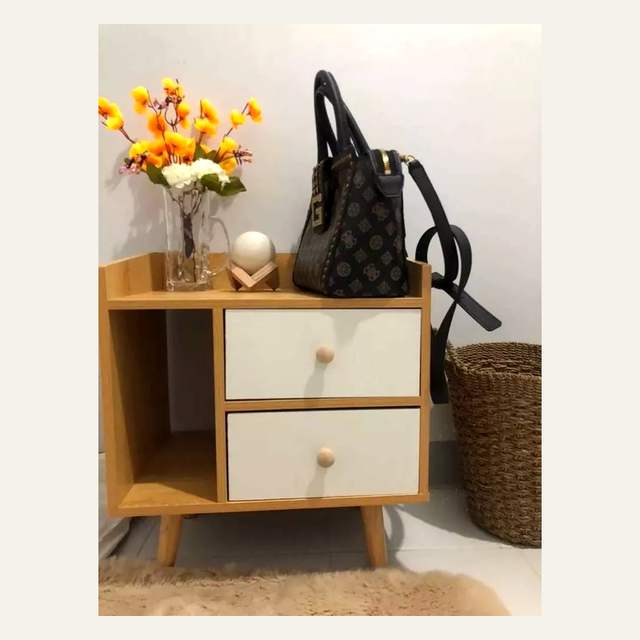 Nakas kayu terang berlaci putih dengan vas bunga dan tas di atasnya di dekat dinding putih.