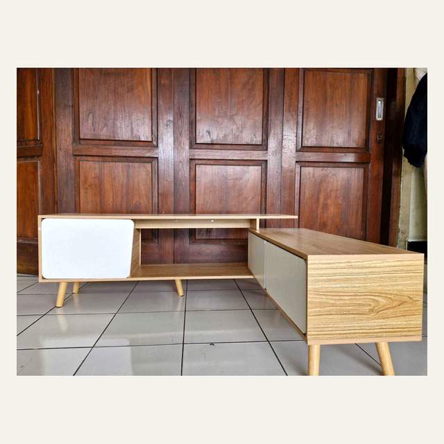 Rak tv kayu terang bertingkat dengan panel putih difoto menyerong di depan pintu kayu.